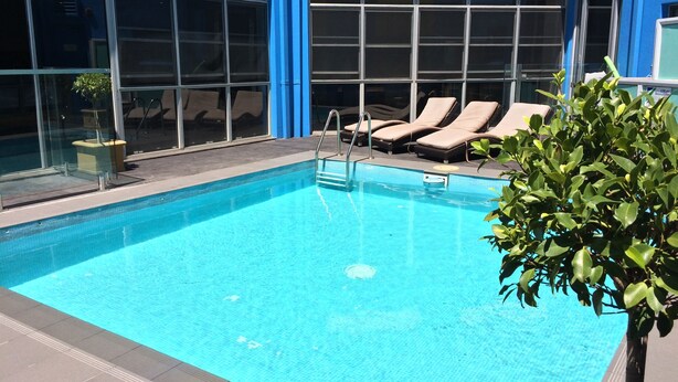 A swimming pool with lounge chairs and a glass wall. - Sydney Student Living - Hostel (Concord)