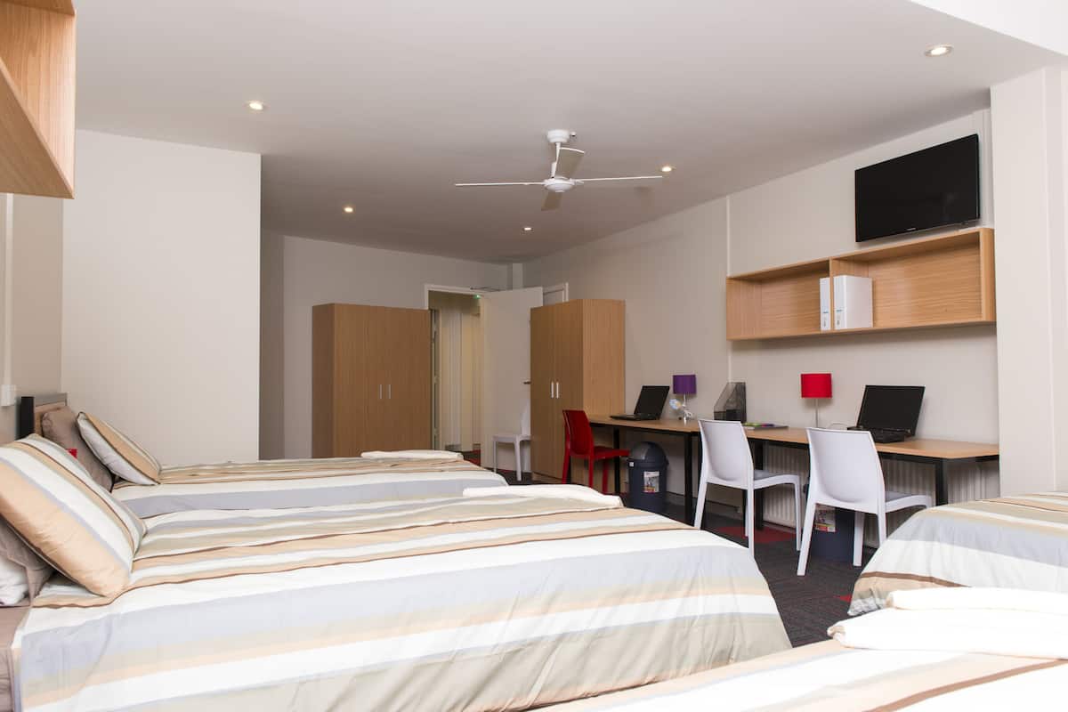 Una habitación de hotel con dos camas, un escritorio con computadora y un televisor en la pared.