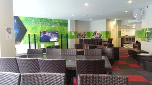 A Sydney Student Living lounge with wicker furniture, a TV screen, and green and white decor. - Sydney Student Living - Hostel (Concord)
