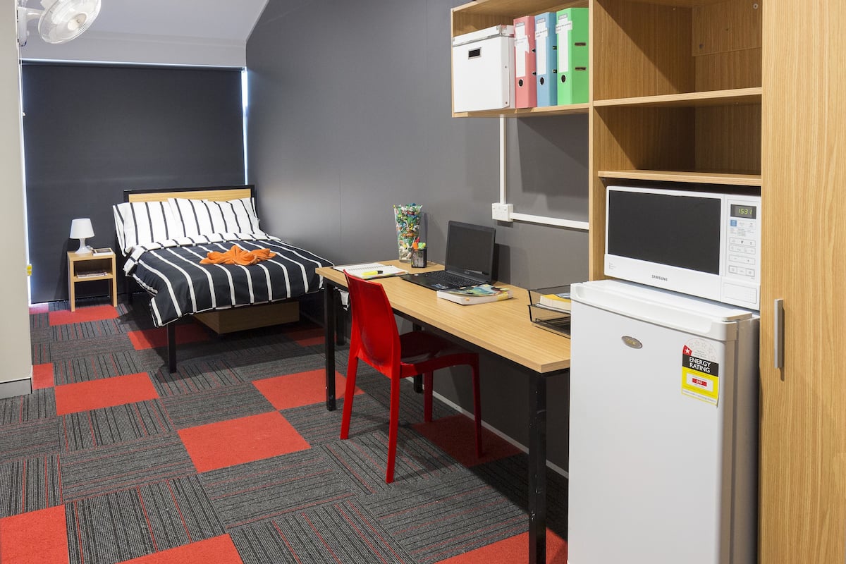 Un dormitorio con cama, escritorio, silla y refrigerador.