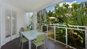 A covered outdoor area with a table and chairs, surrounded by lush greenery and a view of a pool and buildings. - Seascape Holidays- Beaches (Port Douglas)