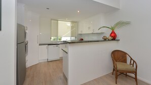 A modern kitchen with white cabinetry, a built-in dishwasher, and a wooden floor. - Seascape Holidays- Beaches (Port Douglas)