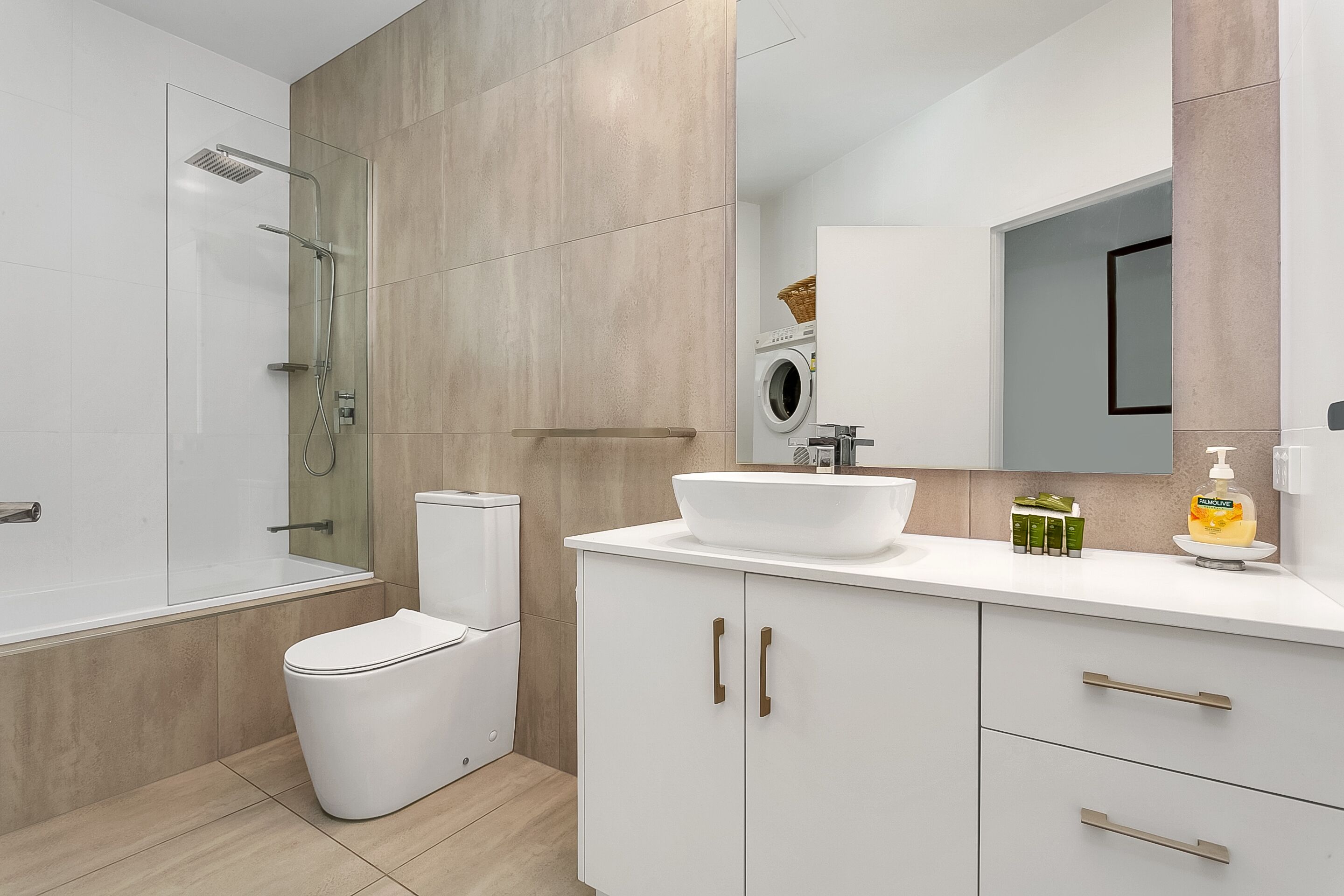 Een moderne badkamer met een douchecabine van glas, een toilet, een wastafel met een grote spiegel en een kast met lades.