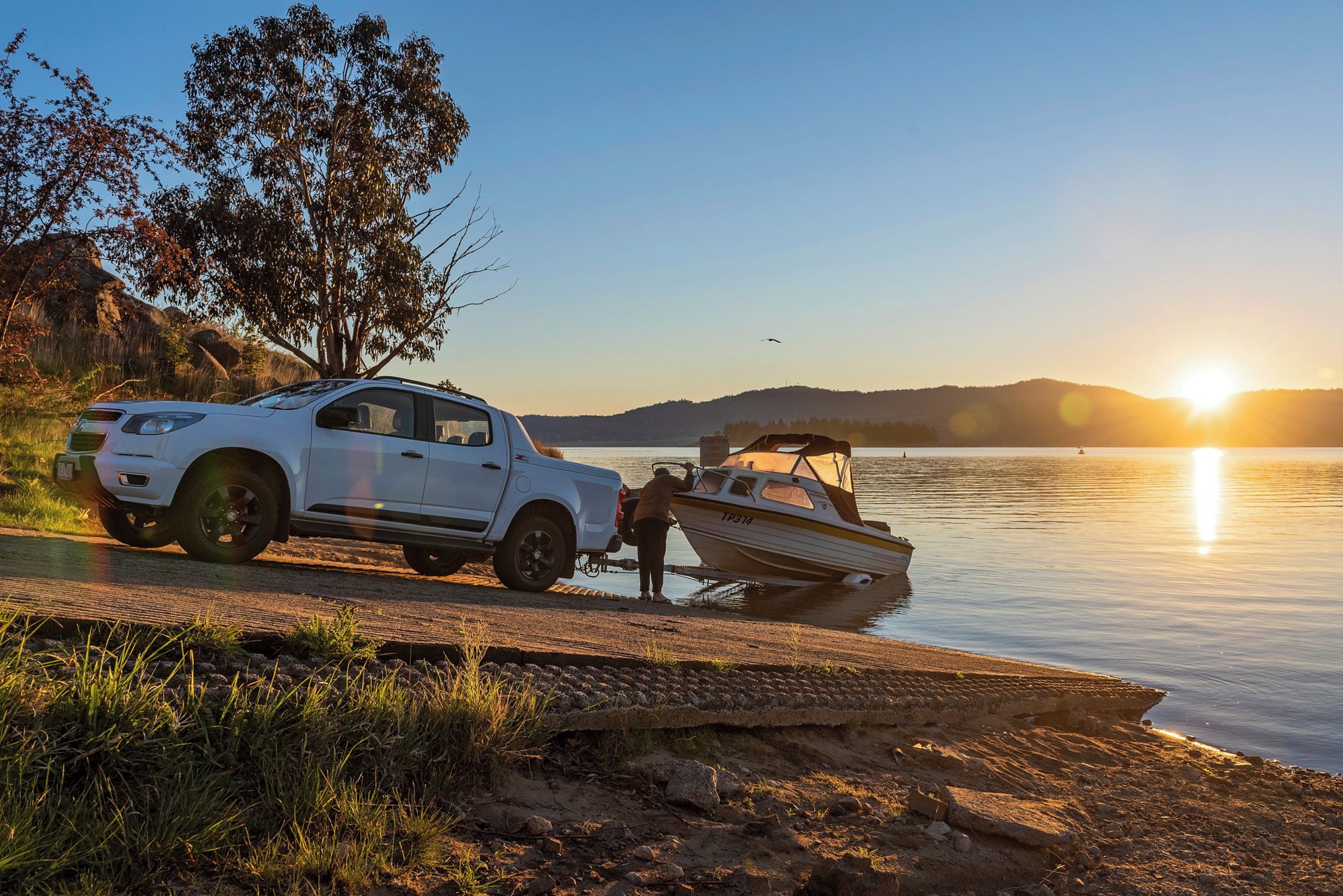Un SUV blanc est garé au bord d’un lac, et un bateau est amarré à proximité.