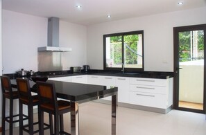 Cocina moderna con una isla grande, armarios blancos y un ventanal con vista a follaje.