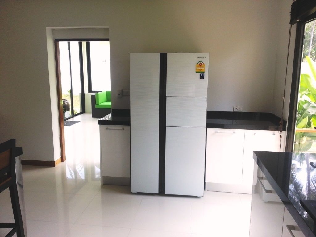 A modern kitchen with a large refrigerator, white cabinets, and a black countertop.