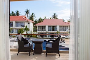A balcony with wicker furniture overlooking a swimming pool and a resort building with a red roof.