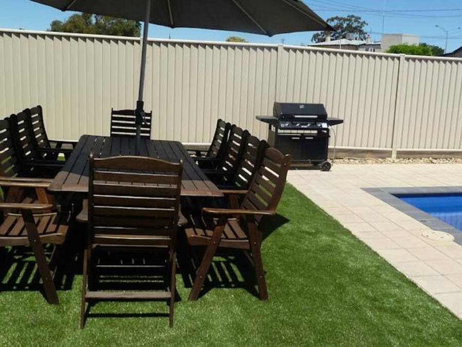 A dining area with a table and chairs, a barbecue grill, and a swimming pool.