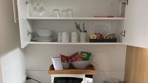 Una kitchenette compacta equipada con microondas, un refrigerador pequeño, un lavamanos y una repisa con cristalería y aperitivos.