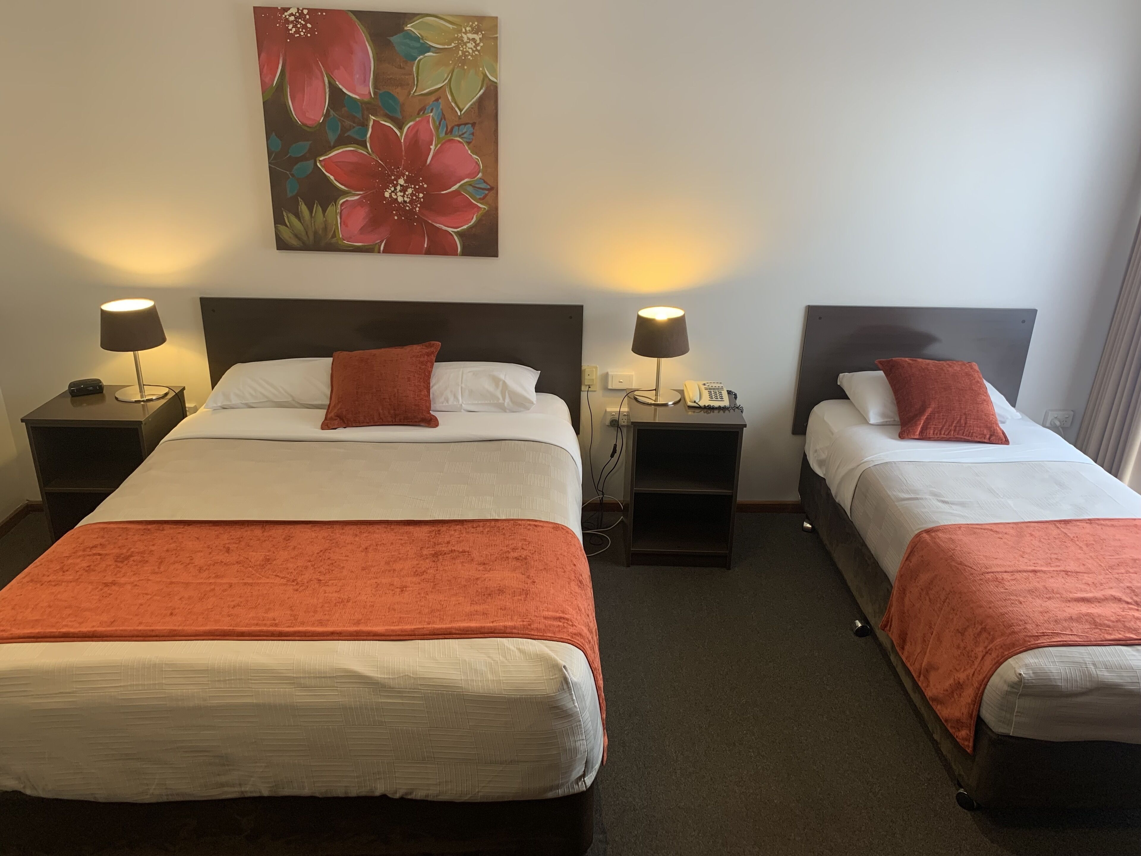 A hotel room with two beds, each with a white bedspread and orange throw pillows. There are two bedside tables with lamps and a painting above the beds.
