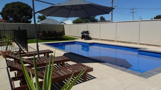 Una piscina con solárium empedrado, zona de barbacoa y mobiliario de exterior.