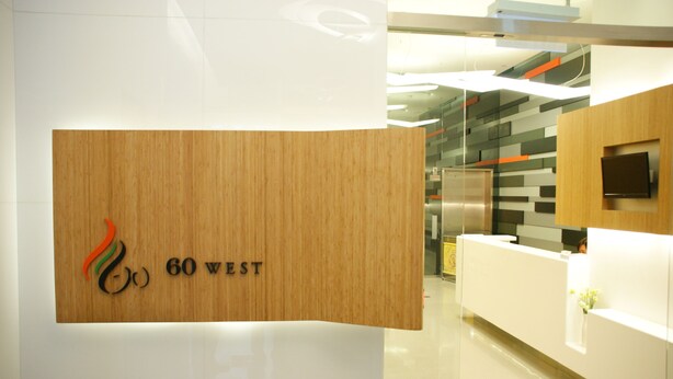 A reception area with a wooden panel displaying the text "60 WEST" and a logo. - 60 West Hotel (Hong Kong)
