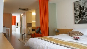 A hotel room with a bed, a desk, and a chair. There is a painting on the wall and a window with curtains. - 60 West Hotel (Hong Kong)