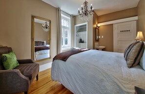 A bedroom with a large bed, a chair, a mirror, a chandelier, and a closet.