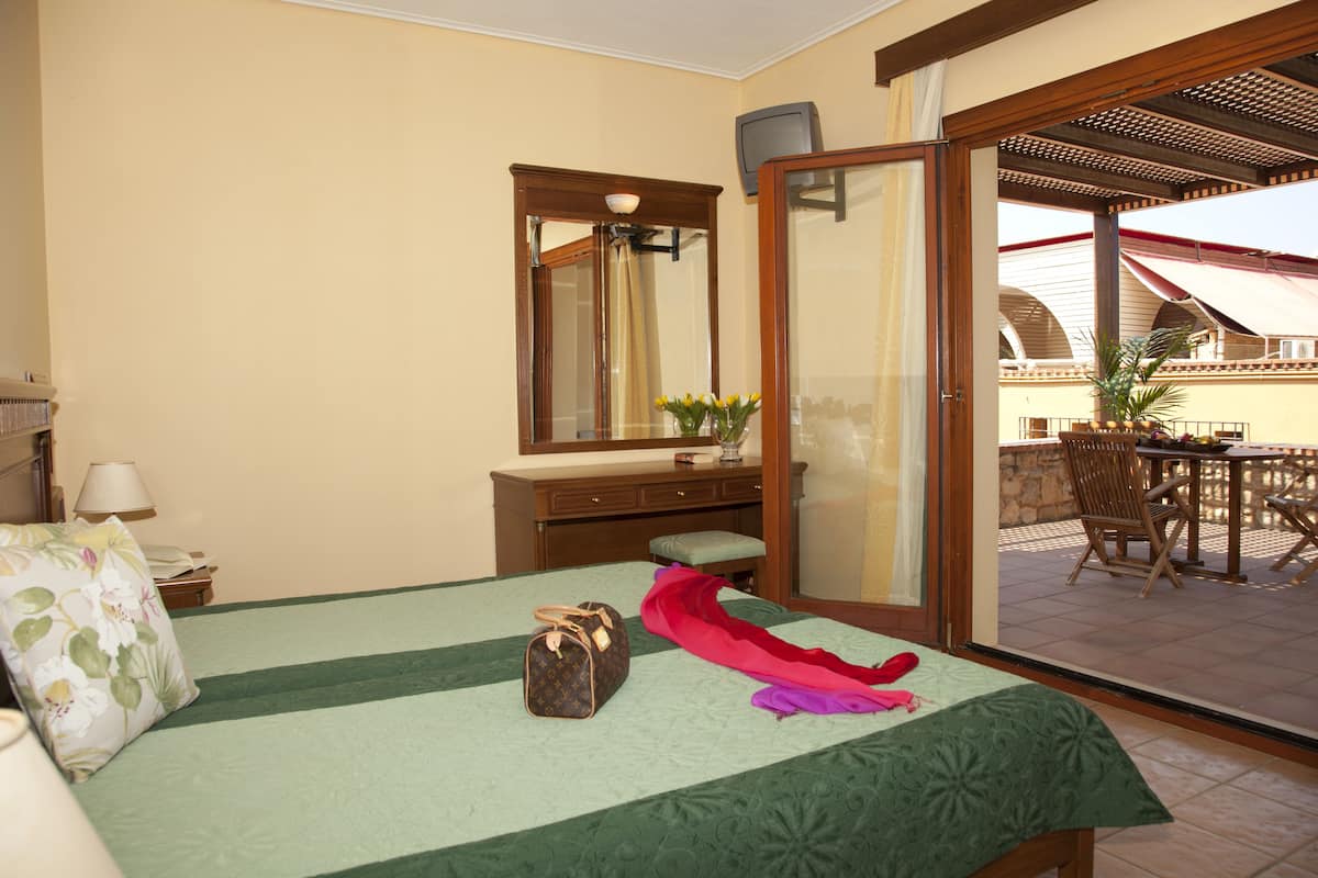 Habitación de hotel con cama, tocador con espejo, una mesita y vista a un patio exterior.