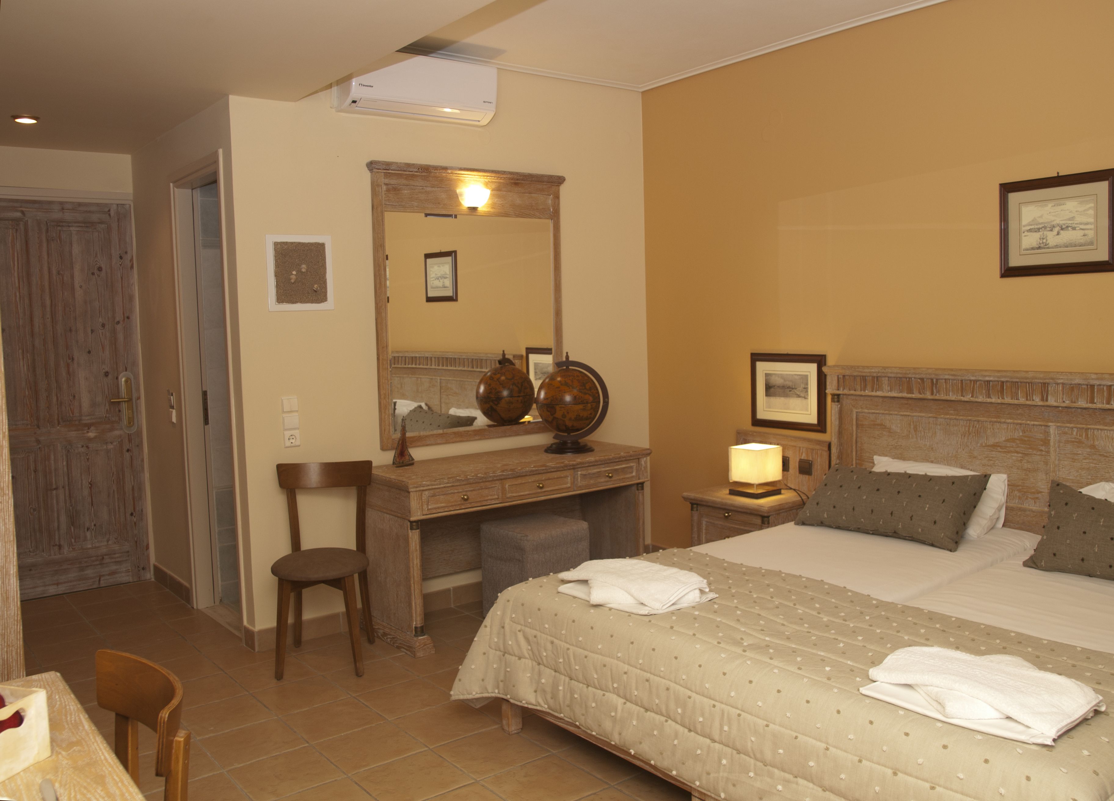 Una habitación de hotel con cama, escritorio, silla, espejo, un globo terráqueo y un cuadro en la pared.