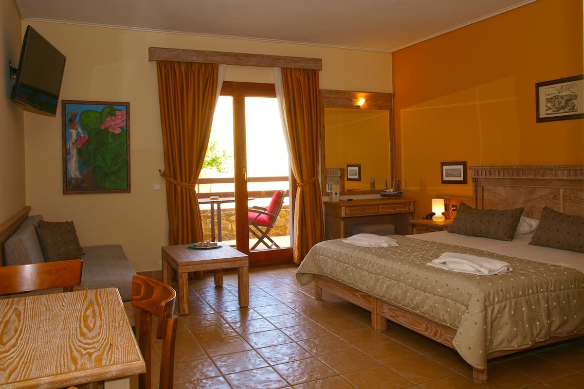 Habitación de hotel con cama, escritorio, silla, mesita y balcón con vistas.