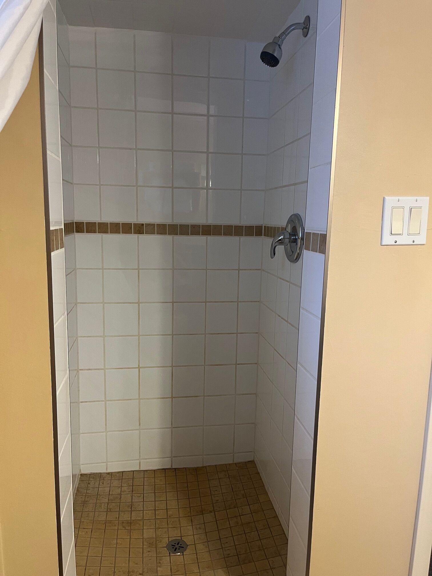 A small, enclosed shower area with white tiles and a brown border.