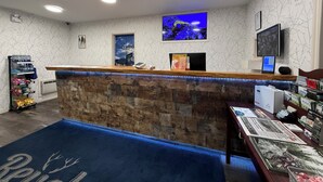 Un comptoir d’accueil avec une façade en pierre, une moquette bleue ornée de motifs de cerfs, un téléviseur fixé au mur et une caméra de surveillance fixée au mur.