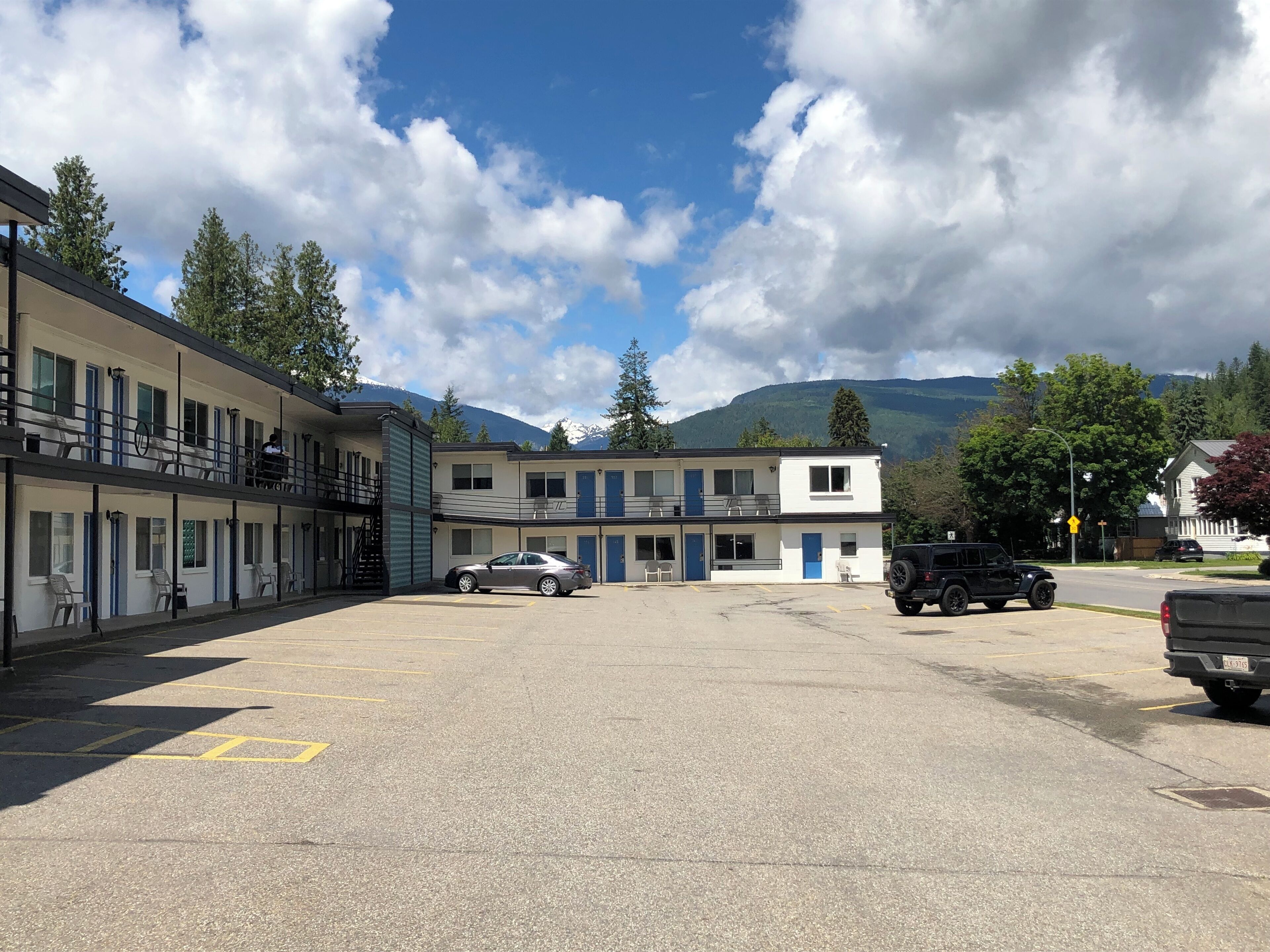 A motel with a two-story structure, a parking lot, and a mountain backdrop.