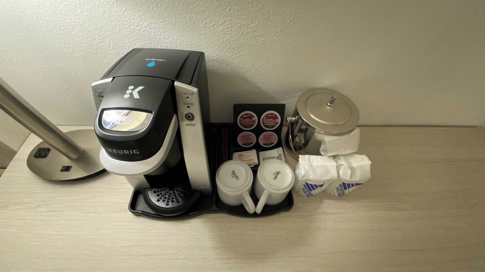 Una cafetera Keurig con depósito de agua, portacápsulas, dos tazas de café y un cesto de basura.