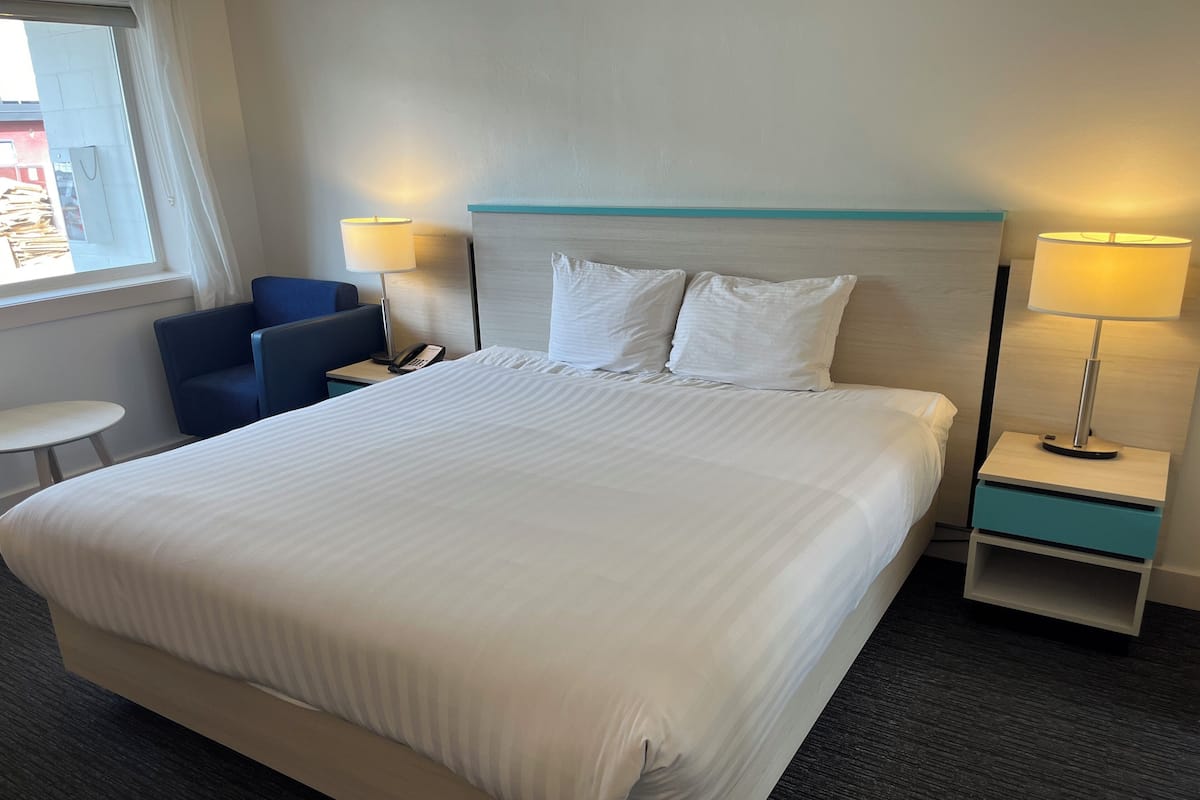 Habitación de hotel con una cama grande, dos mesitas de noche con lámparas, un escritorio pequeño con una silla y una ventana con cortinas.
