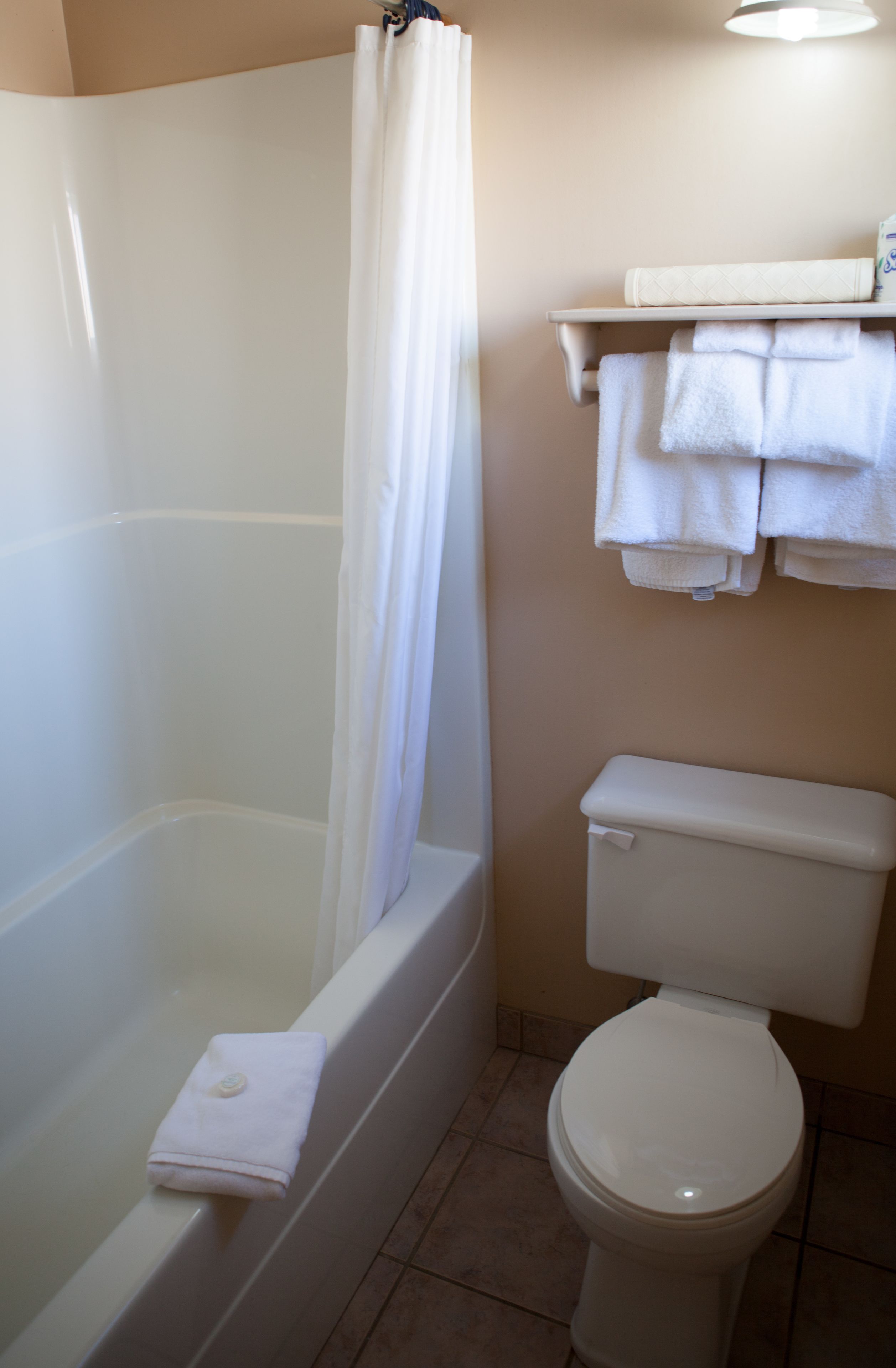 A bathroom with a bathtub, toilet, and a shelf with towels.