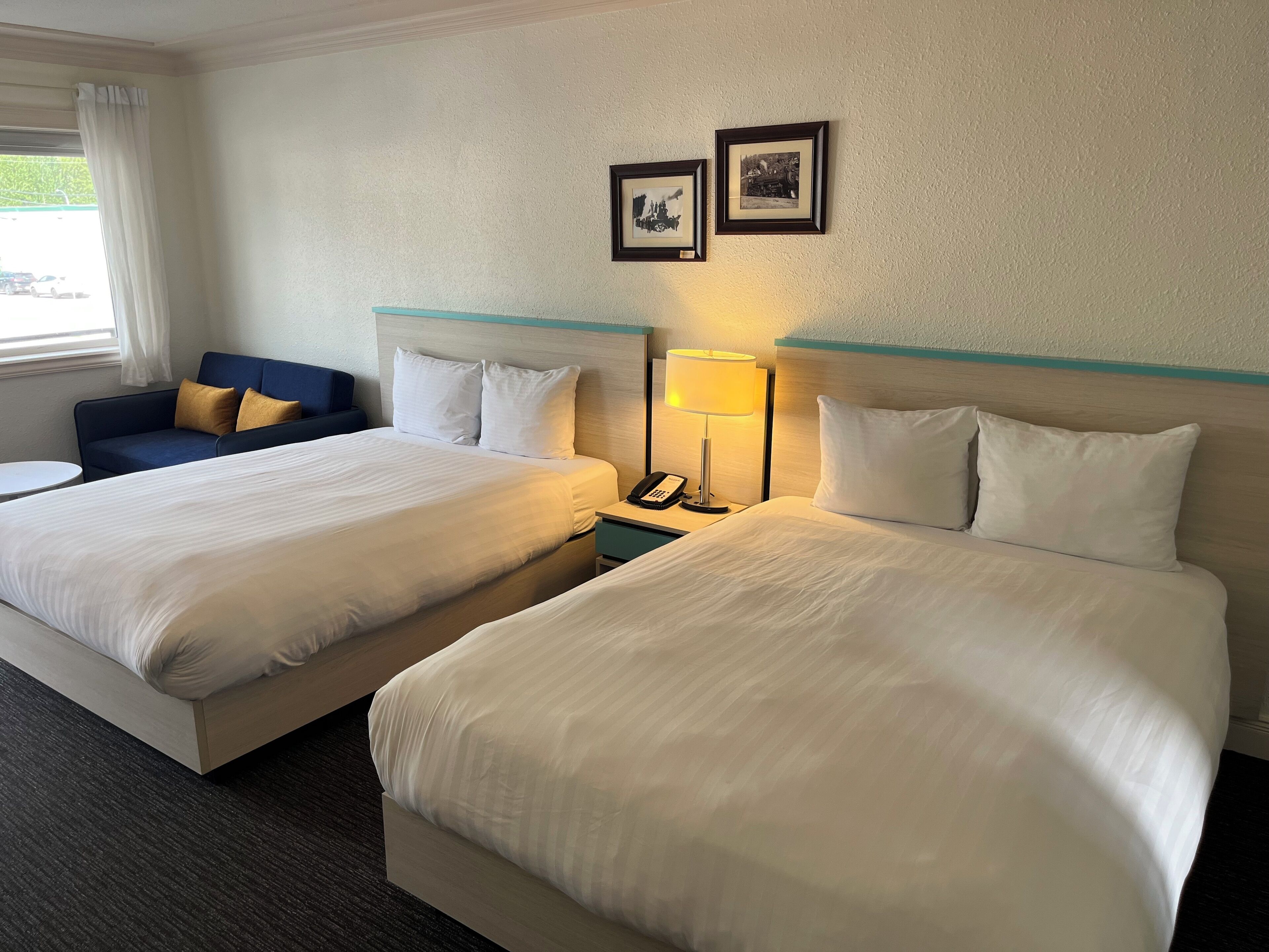 A hotel room with two beds, a desk, a chair, and a window with curtains.