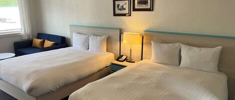 A hotel room with two beds, a desk, a chair, and a window with curtains.