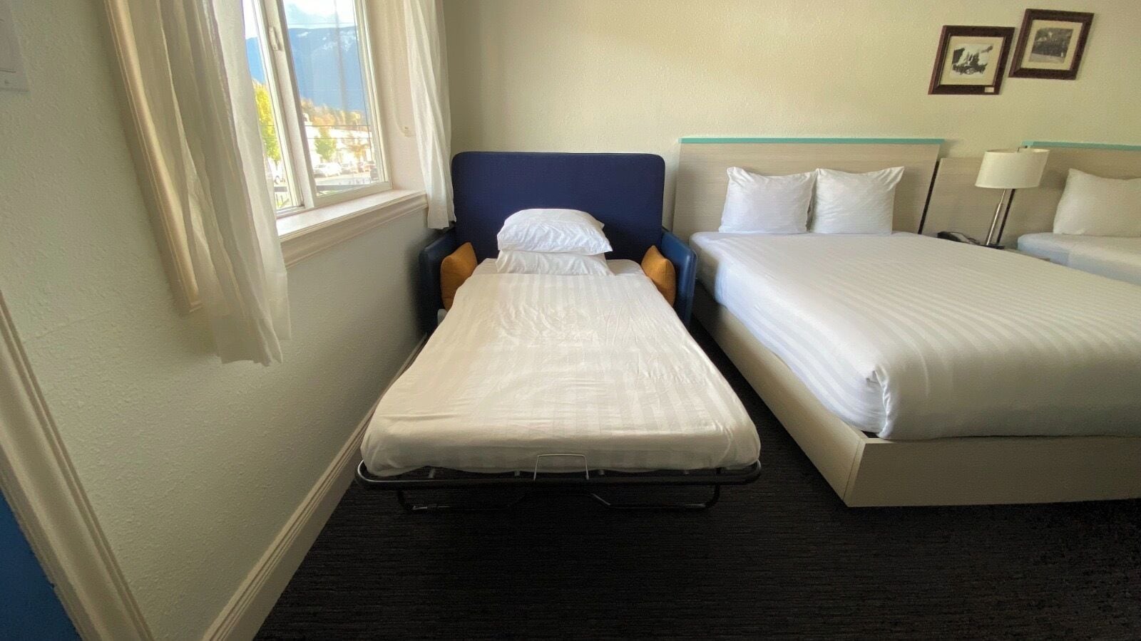 A hotel room with two beds, a window with curtains, and a small table with a lamp.