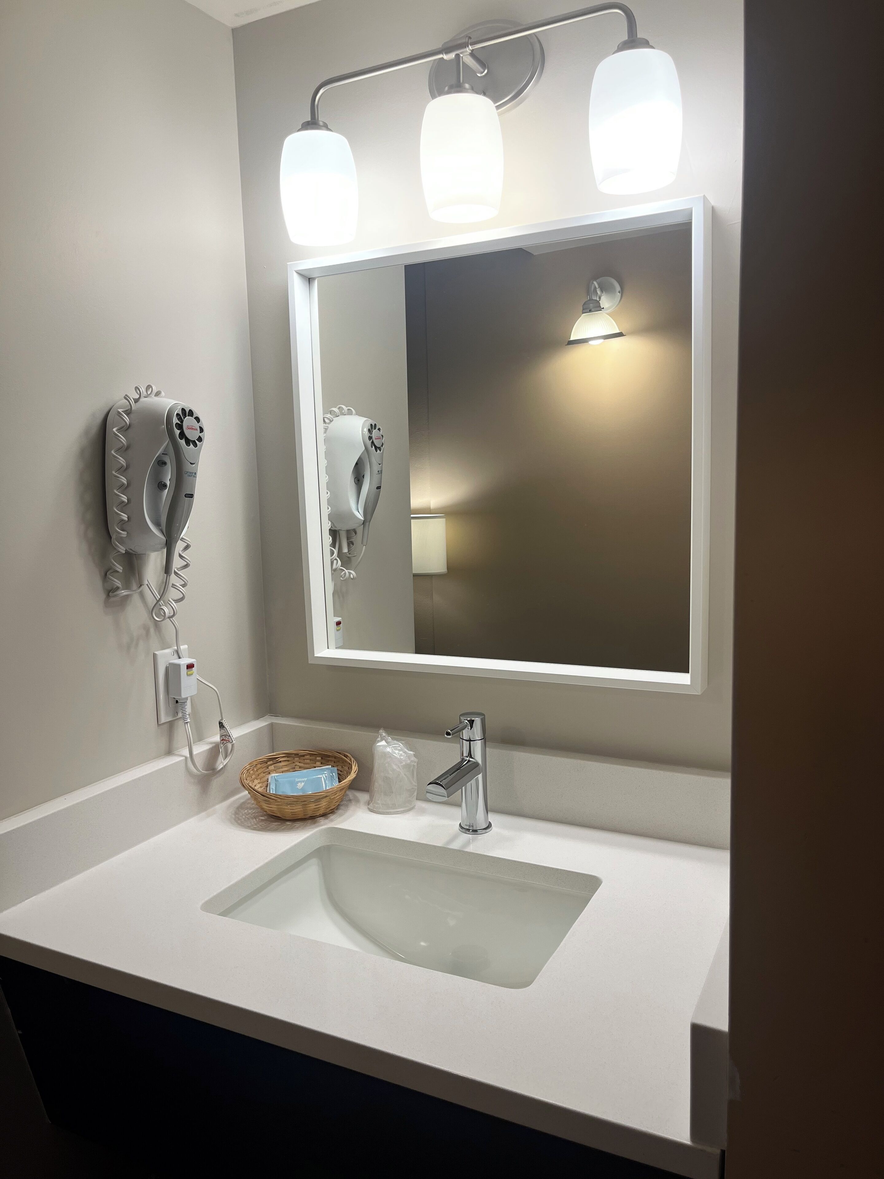 A bathroom with a white sink, a mirror, and two hair dryers mounted on the wall.