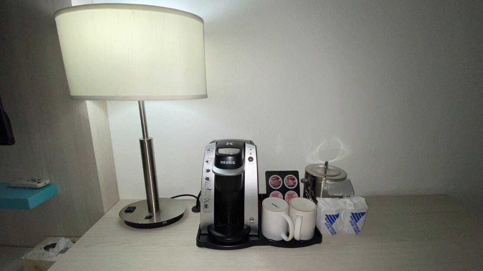 Una cafetera, dos tazas, una caja de pañuelos y una lámpara sobre una mesa.