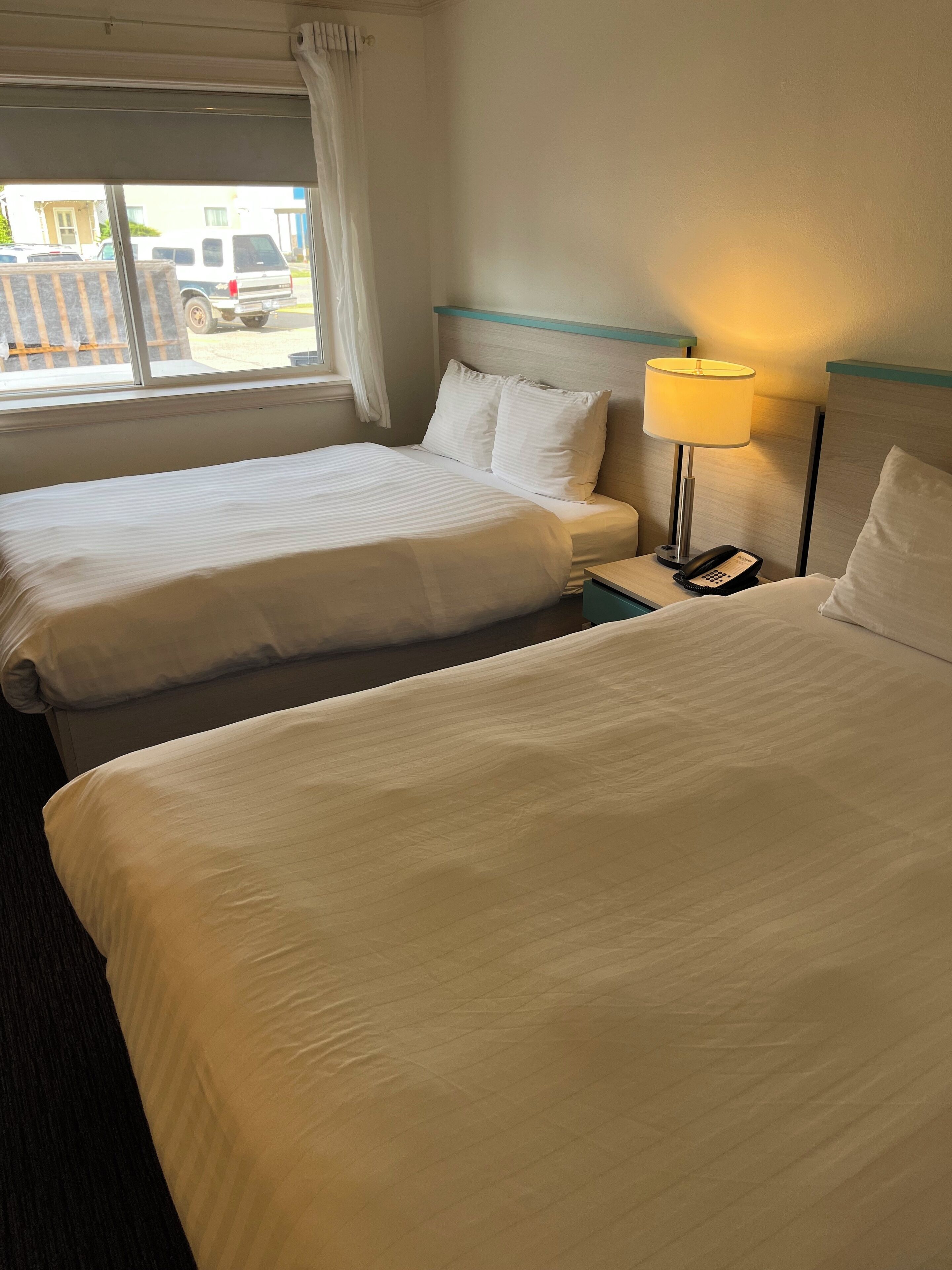 Una habitación de hotel con dos camas, una mesita de noche con lámpara y una ventana con cortinas.