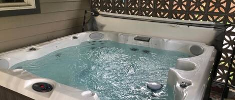 Ein Whirlpool mit Bedienfeld, umgeben von einer Holzterrasse und einem Gitterzaun.