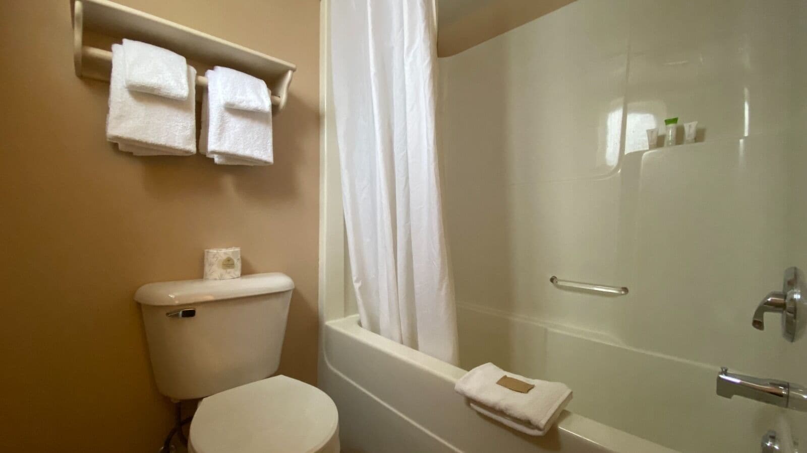 A bathroom with a toilet, a bathtub, and a shower curtain. There are two towels hanging on a shelf above the toilet.