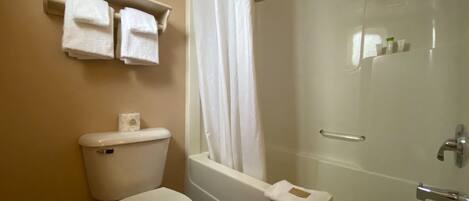 A bathroom with a toilet, a bathtub, and a shower curtain. There are two towels hanging on a shelf above the toilet.