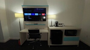 Une chambre d’hôtel équipée d’un bureau, d’un téléviseur à écran plat fixé au-dessus, d’une lampe, d’une machine à café et d’un four à micro-ondes.