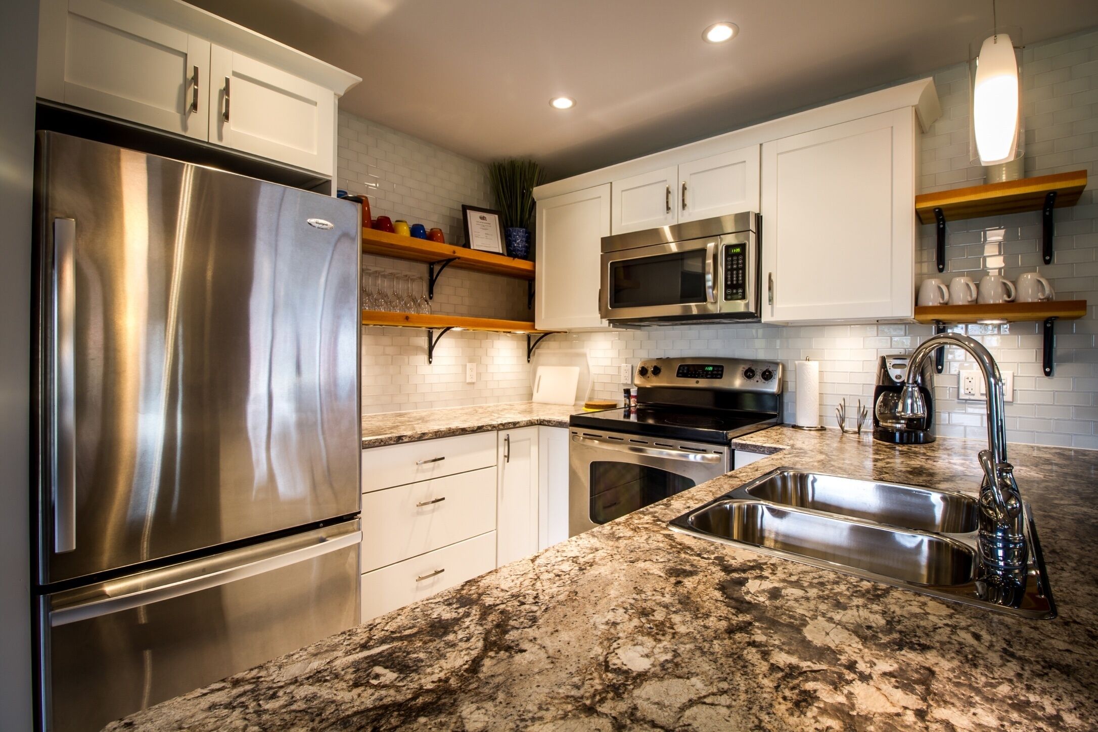 A modern kitchen with stainless steel appliances, white cabinets, granite countertops, and built-in shelving.