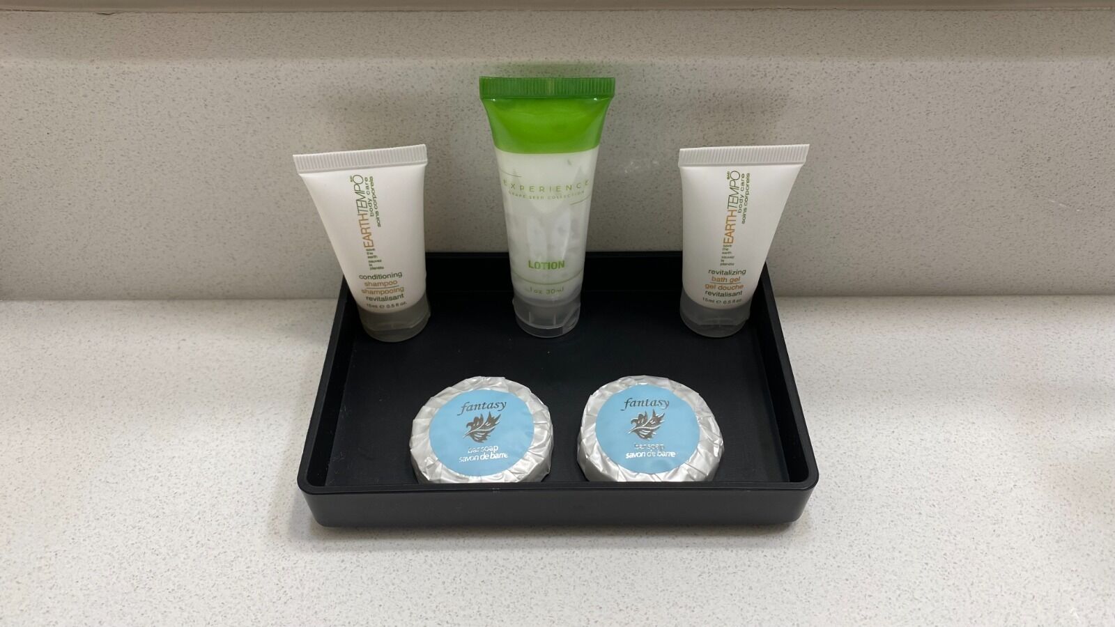 A black tray with three toiletry items: two tubes of lotion and one bottle of shampoo. Below the tray, there are two round containers labeled 'fantasy'.