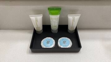 A black tray with three toiletry items: two tubes of lotion and one bottle of shampoo. Below the tray, there are two round containers labeled 'fantasy'.