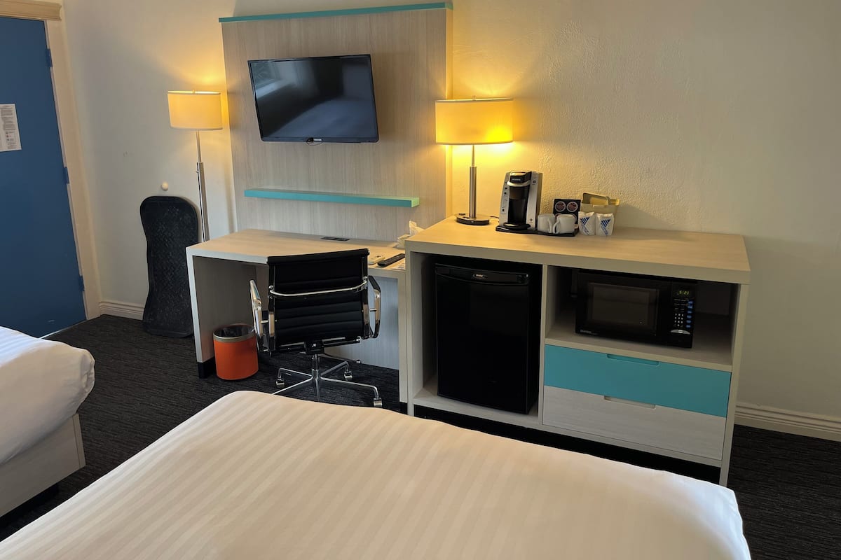 Habitación de hotel con cama, escritorio, televisor de pantalla plana, cafetera, microondas y cesto de basura.