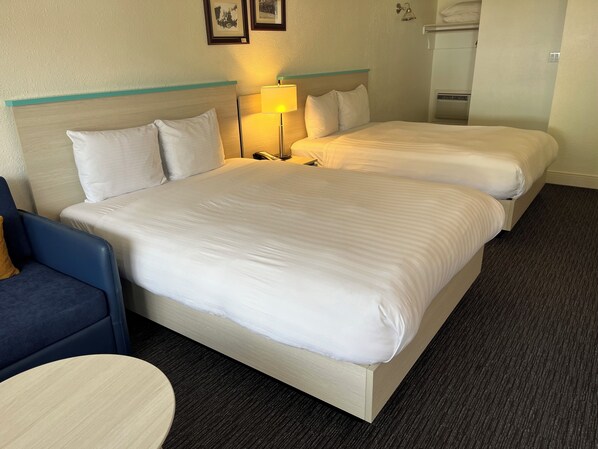 Una habitación de hotel con dos camas, un escritorio, una silla y una lámpara.