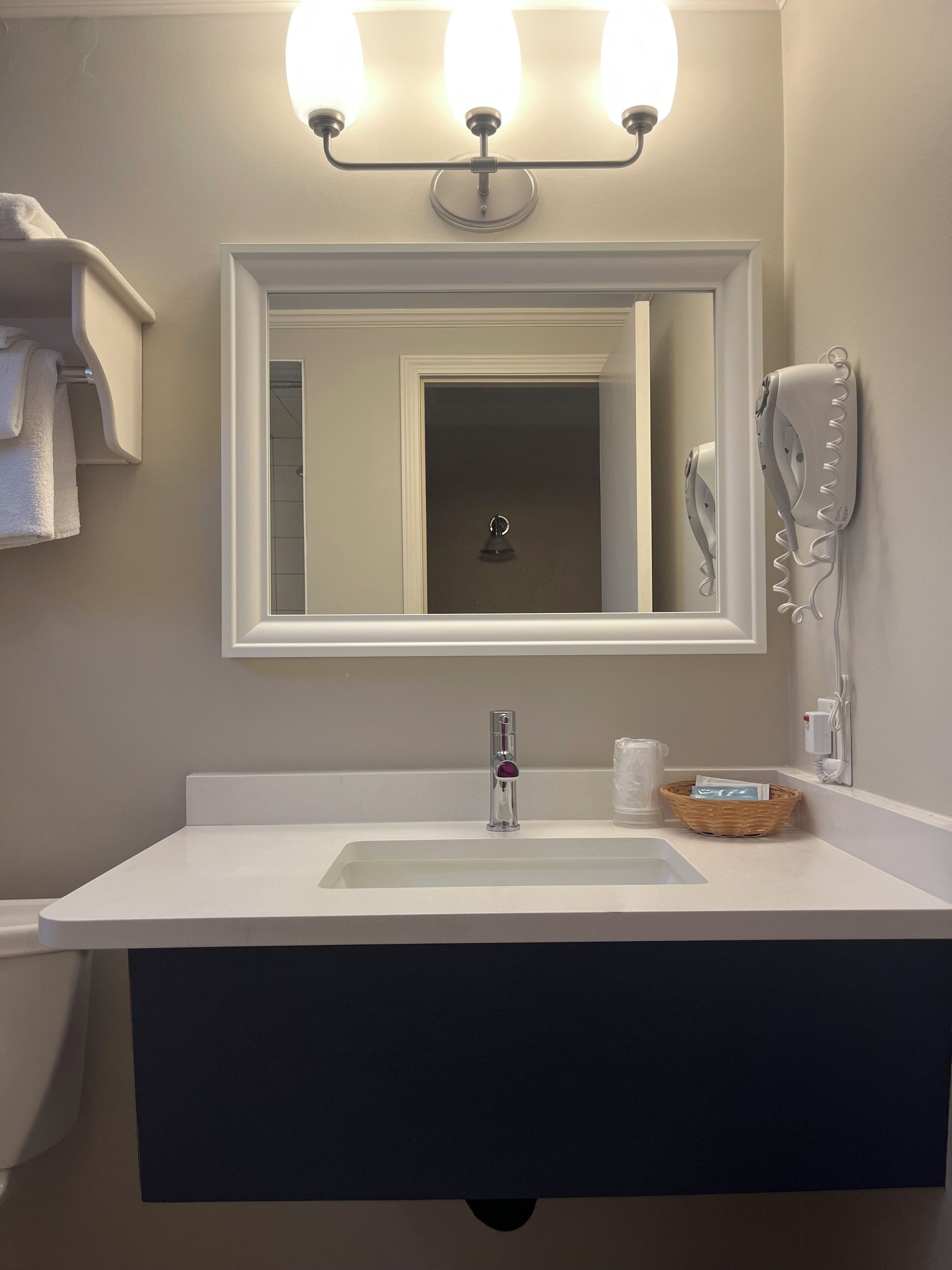 Een badkamer met een witte wastafel, een spiegel, een haardroger en een handdoekhouder.