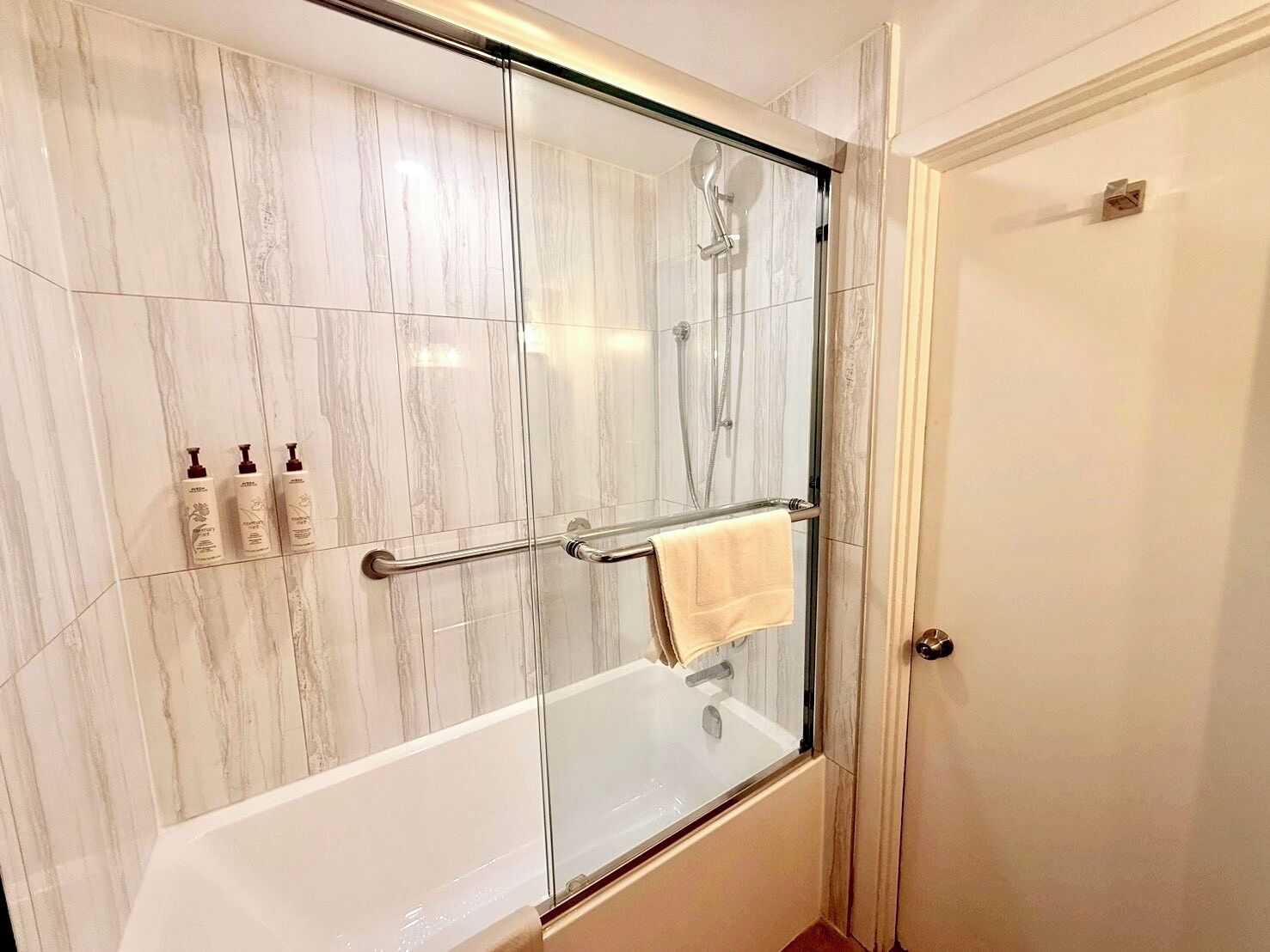 A bathroom with a glass-enclosed shower, a white bathtub, and a towel rack.