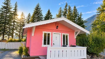 A pink cabin with a white porch, a door, and a window.