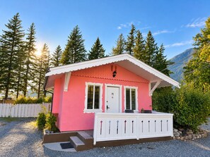 A pink cabin with a white porch, a door, and a window. - Richca Chalets Resort (Hope)