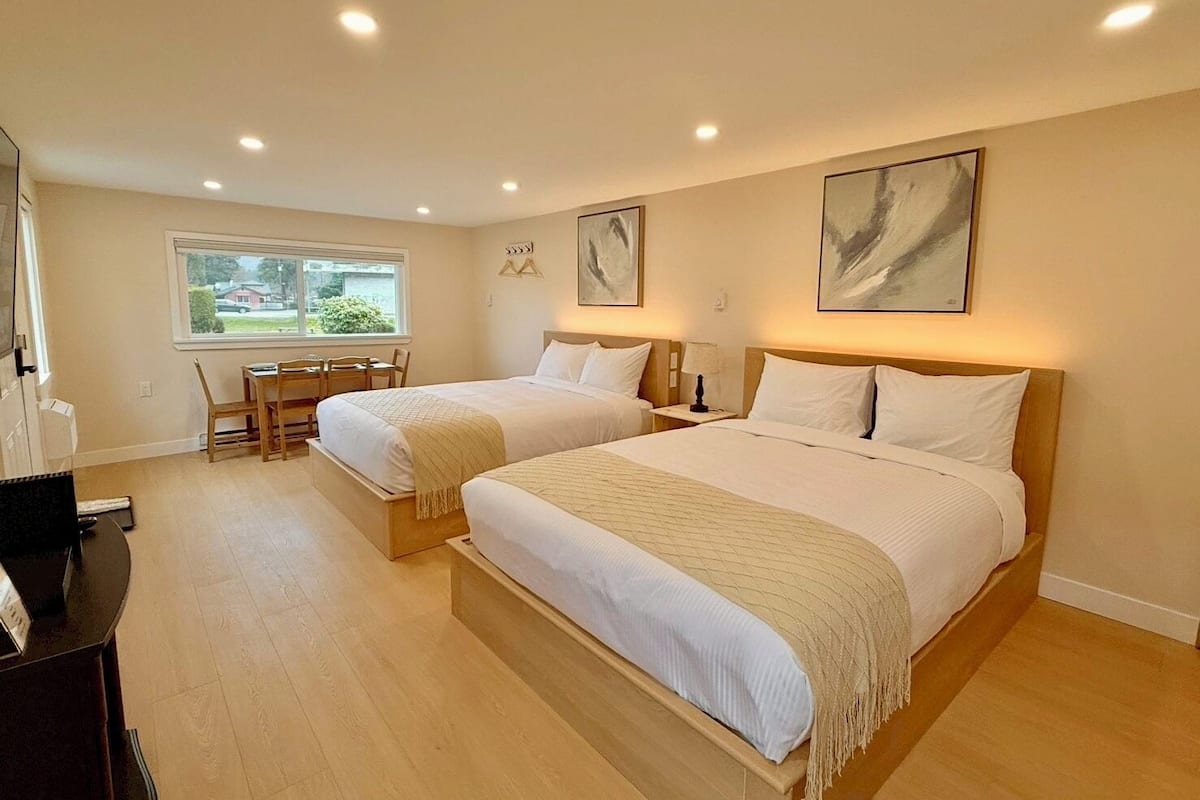 A hotel room with two beds, a desk, and a window.