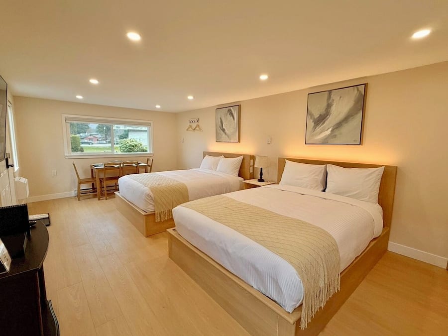 A hotel room with two beds, a desk, and a window.