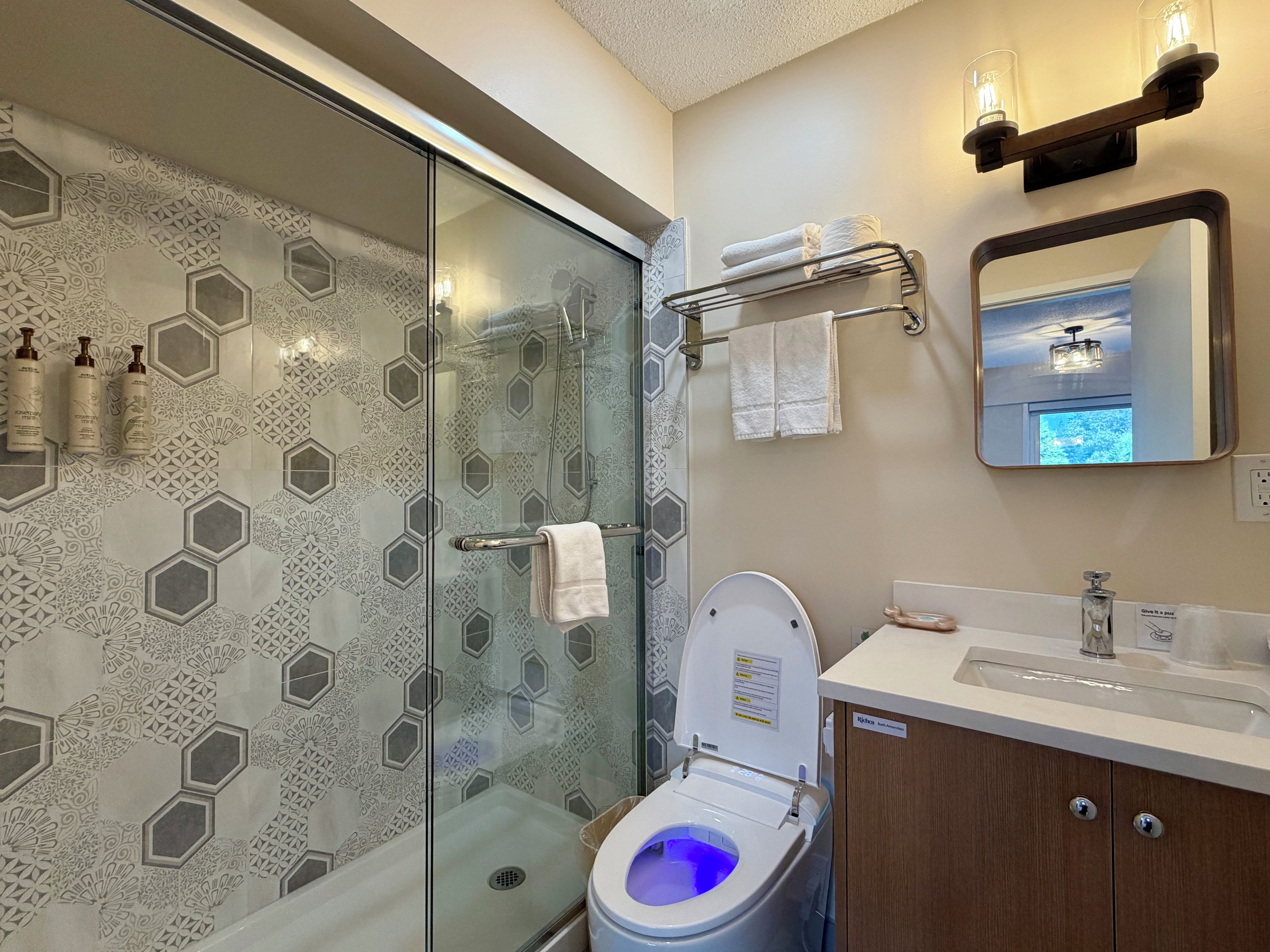 A modern bathroom with a glass-enclosed shower, a toilet with a blue light, and a vanity with a mirror and towel rack.