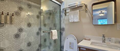 A modern bathroom with a glass-enclosed shower, a toilet with a blue light, and a vanity with a mirror and towel rack.